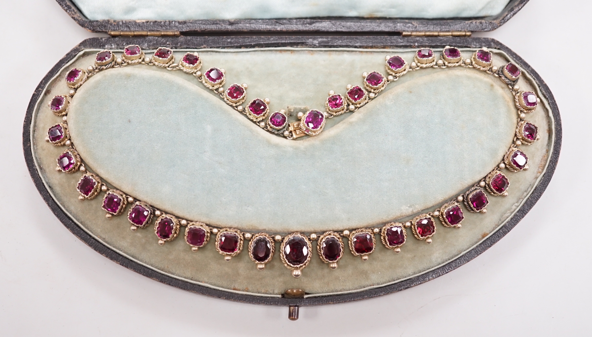 A cased 19th century gilt white metal and graduated oval and square cut garnet set fringe necklace, lacking drop, 37cm.